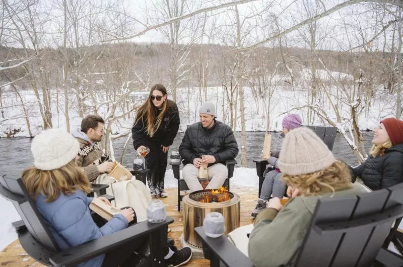 A group of people sit by an outdoor firepit in the winter.