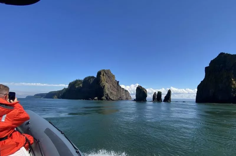 A person takes pictures of cliffs and rock formations from a distance while in a zodiac style boat in the Bay of Fundy.