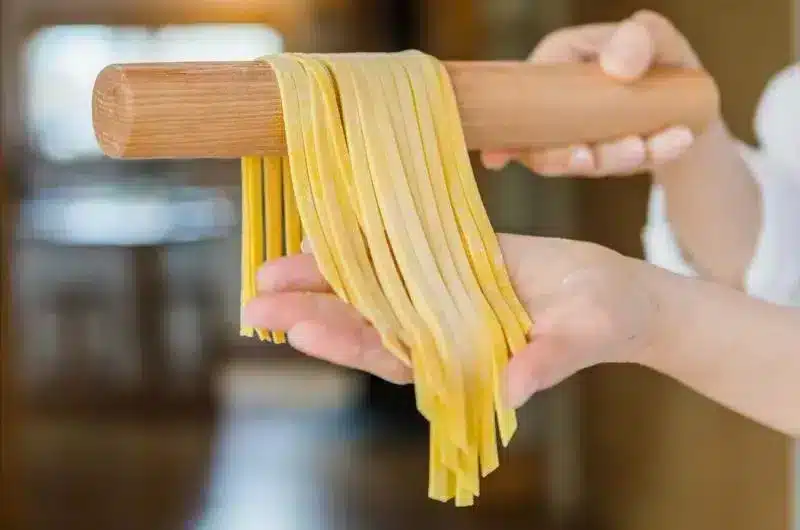 A hand holds out freshly made pasta on a rolling pin.